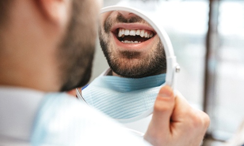 A man looks at his smile in the mirror after receiving his tooth-colored filling