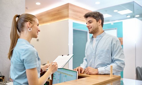 Patient smiling at dental receptionist while reviewing cost
