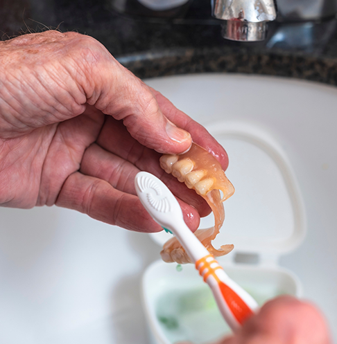 Cleaning a denture in the sink with a toothbrush