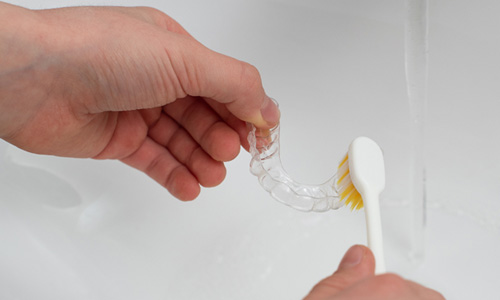 Patient cleaning clear aligner in sink