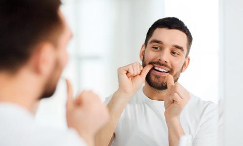 Man flossing his teeth while looking in bathroom mirror