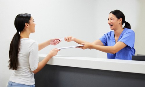 Dental assistant smiling while handing patient forms