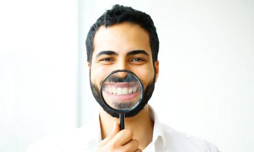 young man using magnifying glass to show off results of teeth whitening in Worcester