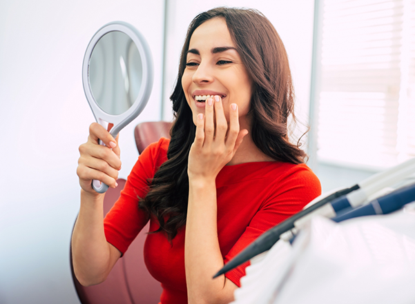 Dental patient in red blouse admiring her smile in mirror