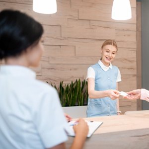 Woman paying smiling dental receptionist for veneers