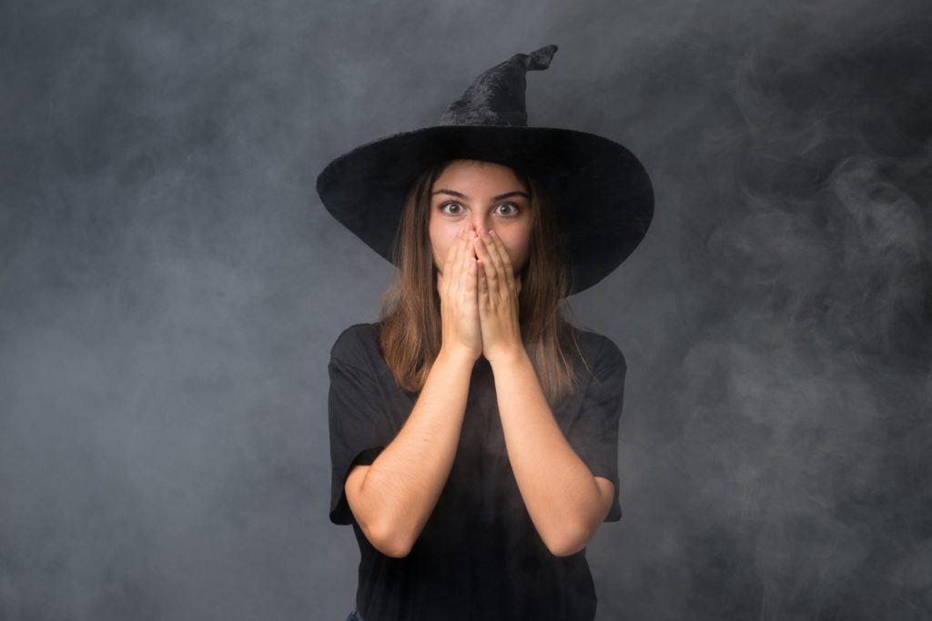 Woman in witch hat covering her mouth in shock