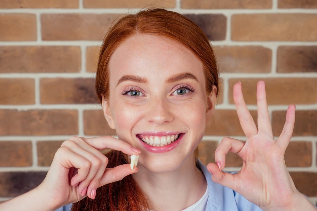 Woman smiling while holding up extracted tooth