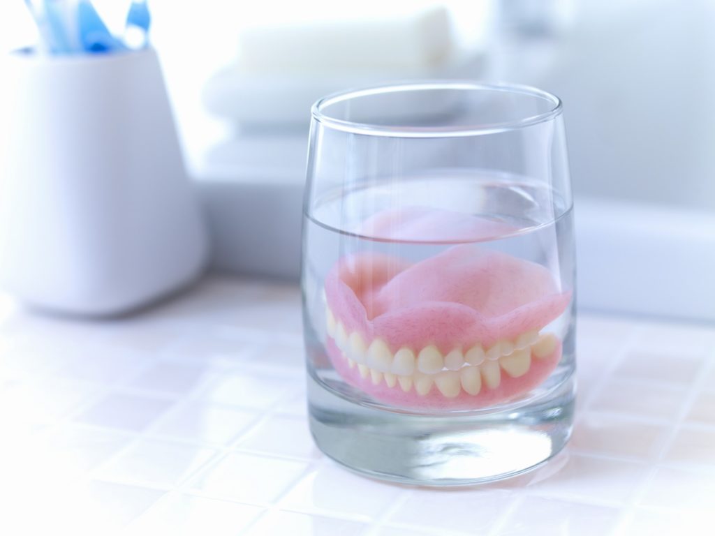 Dentures soaking in glass of denture cleaner on the counter