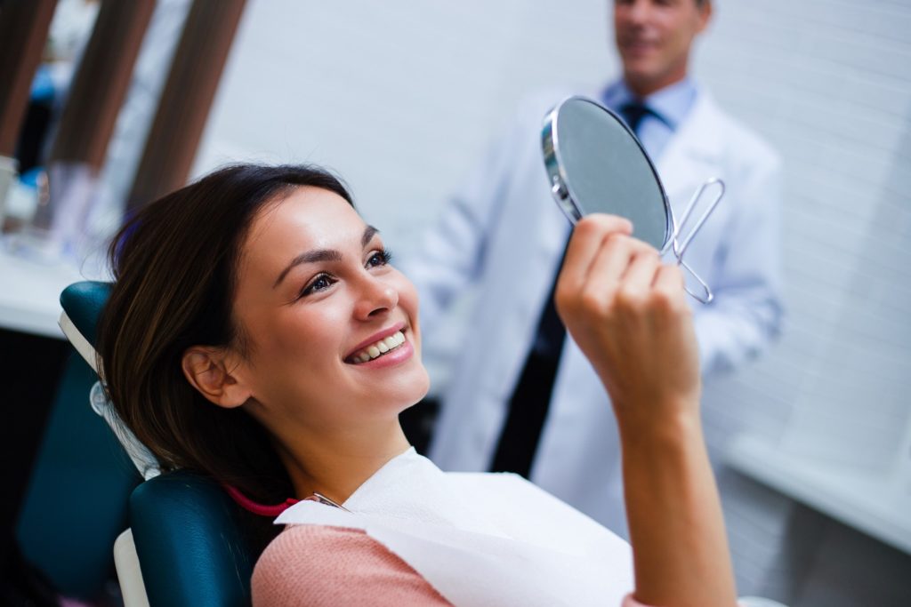 Woman with veneers smiling in dentist's mirror