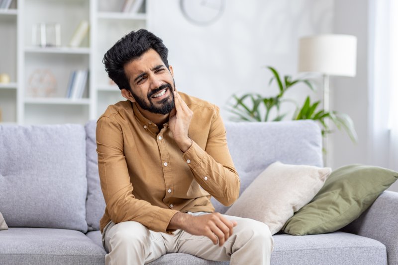 man sitting on a couch and experiencing a dental emergency