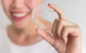 an Invisalign patient smiling and holding their aligner